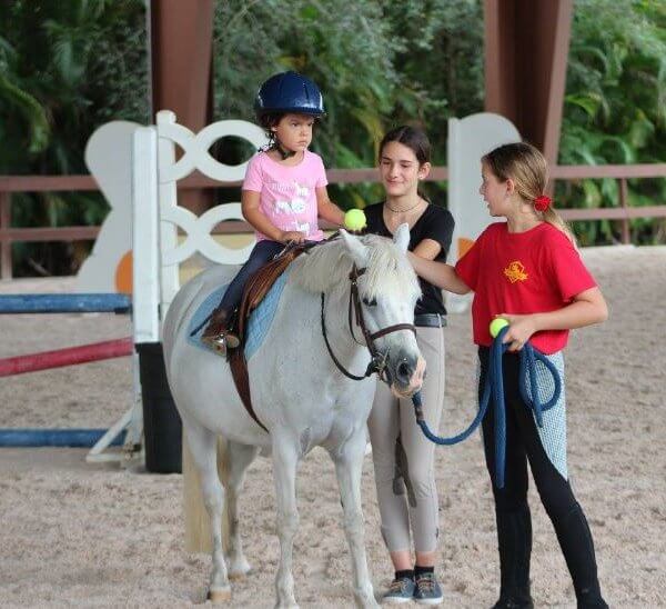 Little kid riding a pony with the help of a camp counselor